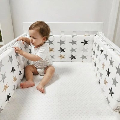 bébé assis dans lit et touche au tour de lit bébé 